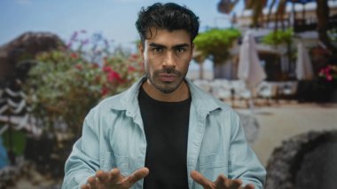 Avuç içleri açık renk kot gömlek giyen İspanyol genç adam gün ışığı altında teras inşaatında yatıştırıcı bir jest olarak yükseltildi..