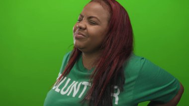 Yeşil tişört giyen gönüllü bir kadın stüdyo çekimlerinde gergin duruş ve çatık kaşlı belini aşağıda tutuyor..