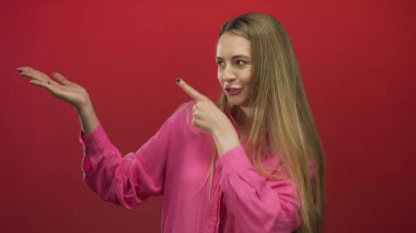 Cesur kırmızı bir arka plana işaret eden, canlı pembe bir gömlek giyen, kendine güveni somutlaştıran ve izole edilmiş bir stüdyoya odaklanan bir kadın..