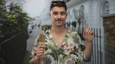 Genç İspanyol bir adam şehirde dondurma yiyor. Çiçekli gömlek ve güneş gözlüğü takıyor. Açık havada neşeli bir turist havasını kucaklıyor..