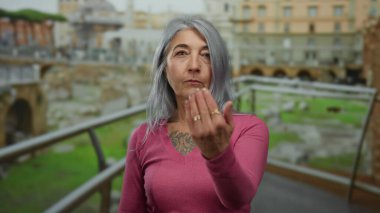 Roma 'daki Roma harabelerinin önünde el kol hareketi yapan yaşlı bir kadın, açık havada antik mimari ve kültür mirasını sergiliyor..