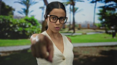 Gözlüklü genç bir kadın güneşli bir parktaki kameraya bakıyor yemyeşil ve açık mavi gökyüzü açık havada neşeli ama odaklanmış bir anı yakalıyor..