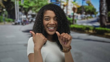 Kadın her iki başparmağı da arkasında hareketli bir caddeye doğru geniş bir gülümsemeyle, iyimserlikle işaret ediyor..