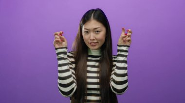 Tırnak işareti yapan bir kadın mor bir arka plana karşı iki eliyle hareket ediyor, çizgili gömlek giyiyor, alaycılık ya da ironi yapıyor, uzun saçlı ve gündelik ifadeli..