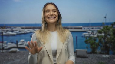 Sahil limanında gülümseyen bir kadın, açık mavi gökyüzünün altında botlar, günlük kıyafetler, sarı saçlar, açık hava manzarası, neşeli bir atmosfer ve canlı bir enerji..