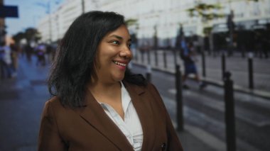 Şehir merkezindeki kalabalık bir sokakta gün ışığında dişlerini gösteren kahverengi ceketli bir kadın gülümsüyor; sevinç iyimserliği.