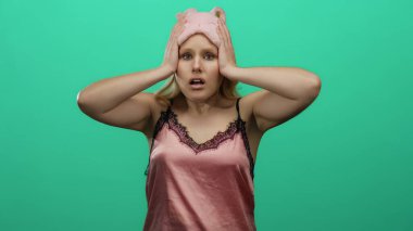 Gecelik giymiş genç sarışın kadın, elleri başının üstünde canlı yeşil bir arka plana yaslanmış, dramatik ve duygusal bir anı yakalıyor..