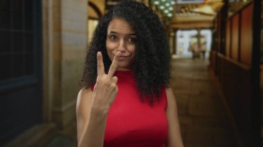 Genç İspanyol kadın gülümsüyor hashtag jesti yapıyor parmakları sokakta kırmızı üstteki ışıklarla aydınlatılıyor; oyuncu bir eğilim.