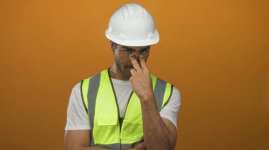 Beyaz şapka ve yansıtıcı yelek giyen genç İspanyol adam ve mühendis stüdyoda kameraya işaret parmağıyla işaret veriyor..