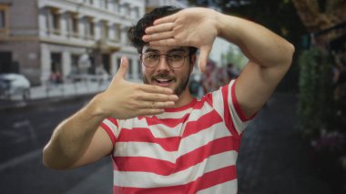 Sakallı, kırmızı çizgili tişörtlü, şehir caddesinde elleri olan, neşeli bir şekilde gülümseyen, güneşli bir gün.