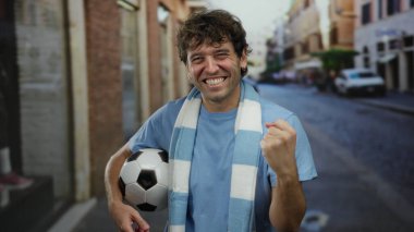 İspanyol bir adam elinde futbol topuyla sokakta kutlama yapıyor, mavi gömlek ve beyaz bir eşarp giyiyor, spor zaferi için sevinç ve heyecan ifade ediyor..