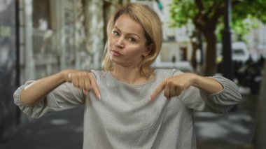 Sarışın kadın, ağaçlar ve sokak lambalarıyla dolu caddeyi işaret ediyor..