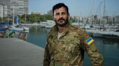 Ukrayna bayraklı İspanyol üniformalı bir adam limana yakın duruyor. Gemileri ve tekneleri var. Deniz manzaralı sakin bir deniz manzarası sergiliyor..