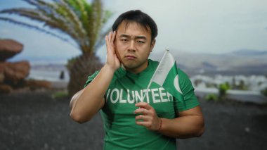 Genç Asyalı gönüllü, Pakistan bayrağını deniz kenarındaki gezinti alanında tutuyor..