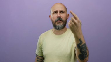 Kel, beyaz, sakallı, parmakları mor arka planda gezen, sıradan gömlekli, kolunda dövmesi olan, izole edilmiş, ciddi bir yüz ifadesi olan bir adam..