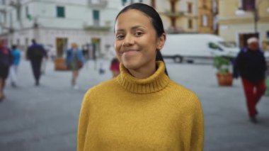 Şehir ortamında bulanık yayalar ve araçlarla kalabalık caddede gülümseyen sarı kazaklı kadın samimi, neşeli ve hayat dolu şehir hayatını yakalıyor..