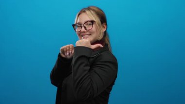 Mavi arka planı işaret eden başparmakları olan, gözlüklü ve siyah takım elbiseli, özgüven ve pozitifliği çağrıştıran, dışa kapalı iletişim odaklı bir kadın..