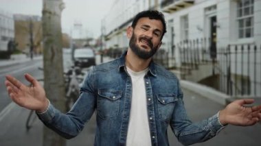 Kot ceketli sakallı bir adam sokakta bisiklet ve arabalarla duruyor, şehir ortamında el çırparken duygularını ifade ediyor..