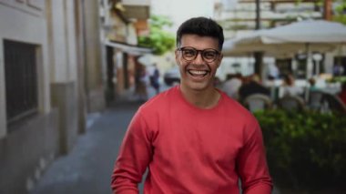Kırmızı kazaklı yakışıklı bir adam şehir caddesindeki terasta gülümsüyor, sıcaklık ve cazibe saçıyor..