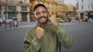 Bisikletler ve bulanık binalarla dolu kalabalık bir şehir sokağında sevinçle yumruklarını sıkan genç adam..