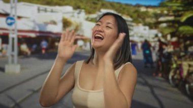 Genç Çinli kadın enerjik bir şekilde şehir sokaklarında neşeli şehir hayatı ile çevrili bir şekilde kutlama yapıyor. Neşesini ve mutluluğunu ifade ediyor. Geniş bir gülümseme ve güneşli gökyüzünün altında kollarını açıyor..