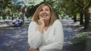 Orman yolunda güneşli yeşil ağaçların arasında yukarı bakarken mutlu bir şekilde gülümseyen kadın. İyimserlik..