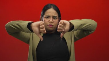 Kırmızı arka planda, gözlüklü ve ceketli bir kadının onaylamadığını belirten bir kadın, izole stüdyo ortamında olumsuz duygular ve ciddi ifadeler sergiliyor..