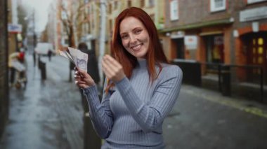 Kızıl saçlı bir kadın elinde İsveç banknotları tutuyor ve şehir sokaklarında iyi bir jest yapıyor. Açık hava ortamındaki zenginlik ve güveni temsil ediyor..