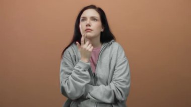 Turuncu arka planda el pençe divan duran bir kadın. Gri kapüşonlu, düşünceli bir yüz ifadesi sergiliyor. Düşünce ve iç gözlem yapıyor..