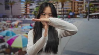 Genç Çinli bir kadın güneşli bir sahil sahilinde renkli şemsiyeler ve arka planda görünen palmiye ağaçları ile mola veriyor..