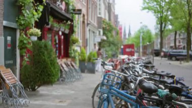 Bulanık yayalar ve renkli binalarla dolu canlı bir Amsterdam caddesi boyunca dizilmiş odaksız bisikletler klasik bir Flaman kentsel ortamı yaratıyor..