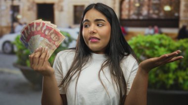 Yoğun bir sokakta, kafası karışık bir ifadeyle Kolombiya pesolarına bakan kadın, mali kararları ve günlük işlemlerdeki belirsizlikleri simgeliyor..