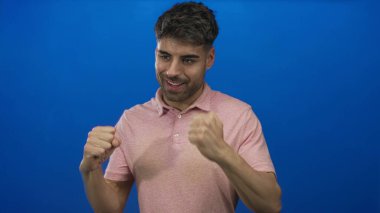 Parlak mavi bir stüdyoda yumruklarını sıkmış ve geniş bir gülümsemesi olan genç bir adam. Gurur güveni hırsı motivasyonu..