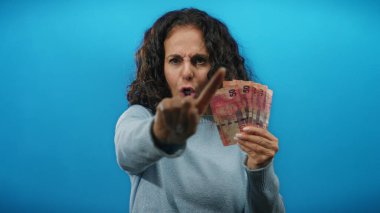 Öfkeyle el kol hareketi yapan bir kadın, Güney Afrika banknotlarını mavi duvara dayayıp para durumuyla ilgili hayal kırıklığını gösteriyor..