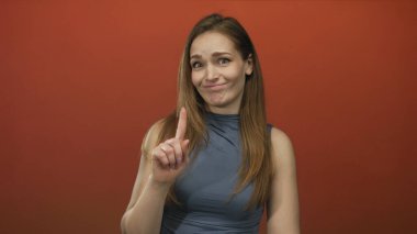 Kafası karışmış genç beyaz kadın kırmızı stüdyo ortamında parmak göğse işaret ediyor. Kendinden şüphe ediyor..