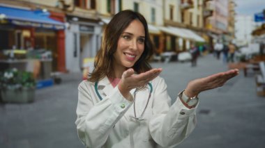 Doktor açık havada elleriniz açık sunum yapıyor, steteskop takmış bir caddede gülümsüyor, şehir ortamında profesyonellik ve güven gösterisi yapıyor..