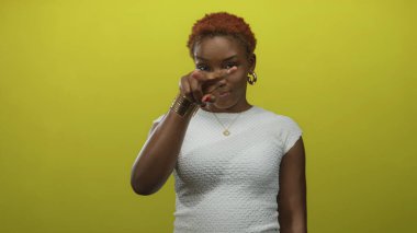 Genç Afro-Amerikalı kadın, sarı stüdyo arka planına parmak işareti yapıyor..