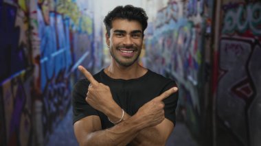 Gülümseyen genç adam sokaktaki canlı grafiti duvarlarını işaret ediyor. Güven şevki..