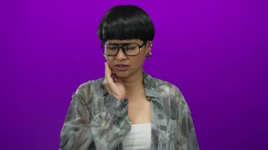 Dişi ağrıyan bir kadın, mor arka planda acı dolu bir ifadeyle yanağını tutuyor.