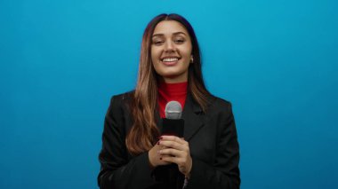 İspanyol kadın muhabir canlı mavi bir arka plana karşı elinde bir mikrofon tutarken özgüvenle gülümsüyor, yayıncılıktaki profesyonellik ve coşkuyu somutlaştırıyor..