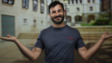 Sokakta sakallı İspanyol bir adam sorgulama jestinde elleri açık duruyor, bulanık şehir geçmişiyle kameraya güvenle gülümsüyor..
