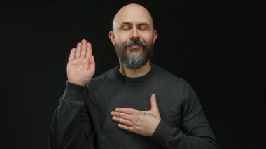 Kel, koyu renk gömlekli bir adam elini göğsüne koyuyor. Siyah bir arkaplana yaslıyor. Samimiyet ve kendine güveni izole stüdyo ortamında resmediyor..