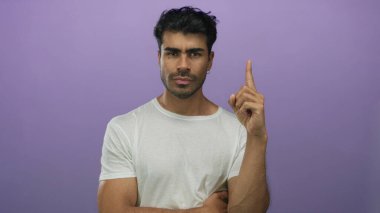 Beyaz tişörtlü bir adam işaret parmağını ciddi bakışları ve odaklanmış duruşuyla stüdyoda yukarı kaldırıyor..