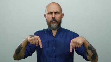 Mavi gömlekli kel adam beyaz arka planda izole edilmiş ciddi bir ifadeyle aşağıya bakıyor.