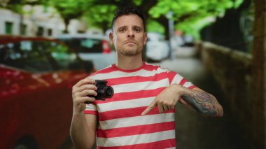 Çizgili gömlekli adam şehir caddesinde bulanık arabaları ve arka planda yeşilliği olan merakla ve keşiflerle dolu bir atmosferi aktarıyor..