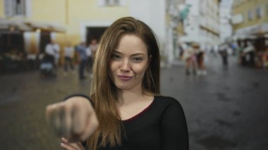 Kalabalık bir şehir caddesinde kameraya doğru elini uzatan genç kadın, dayanışma ve güven eylemlerini güçlendiriyor.