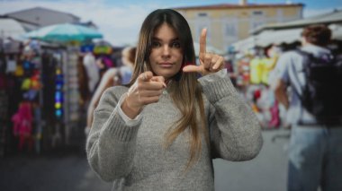 Canlı bir açık hava pazarında, renkli dükkanlar ve arka planda insanlar olan çeşitli sokak yaşamını gözler önüne seren bir kadın kameraya oyuncu bir ezik hareketi yapıyor..