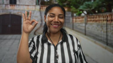 Gülümseyen kadın hakem siyah beyaz çizgili üniforma giyiyor ve ıslık çalıyor..