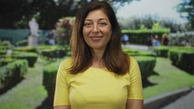 Taştan heykelin yanındaki yeşil bir parkta manikürlü çitlerin yanında gülümseyen orta yaşlı kadın, huzur huzur, neşe ve barış..