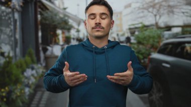 Şehrin dışında bir sokakta mavi bir kapüşonlu giyen, derin ve rahat nefes alan, ağaçlar ve arabalar tarafından görülebilen şehir çevrelerinde yaşayan genç bir İspanyol..